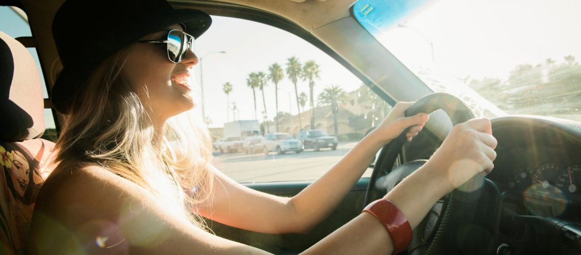 Young woman driving car in sunlight, smiling