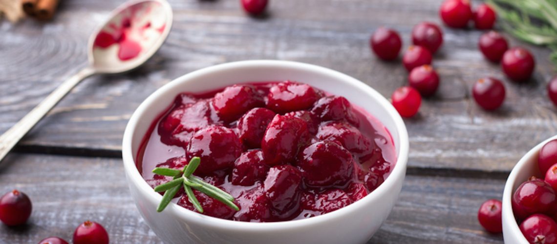 Homemade spicy cranberry sauce with fresh cranberries, cinnamon and star anise on a wooden background