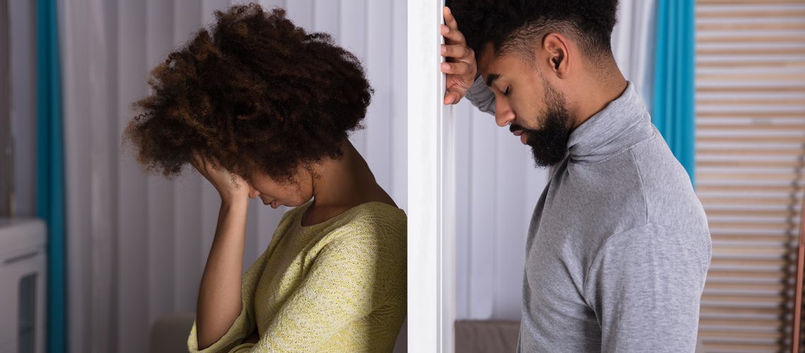 Side View Of Young Unhappy Couple Standing Back To Back At Home